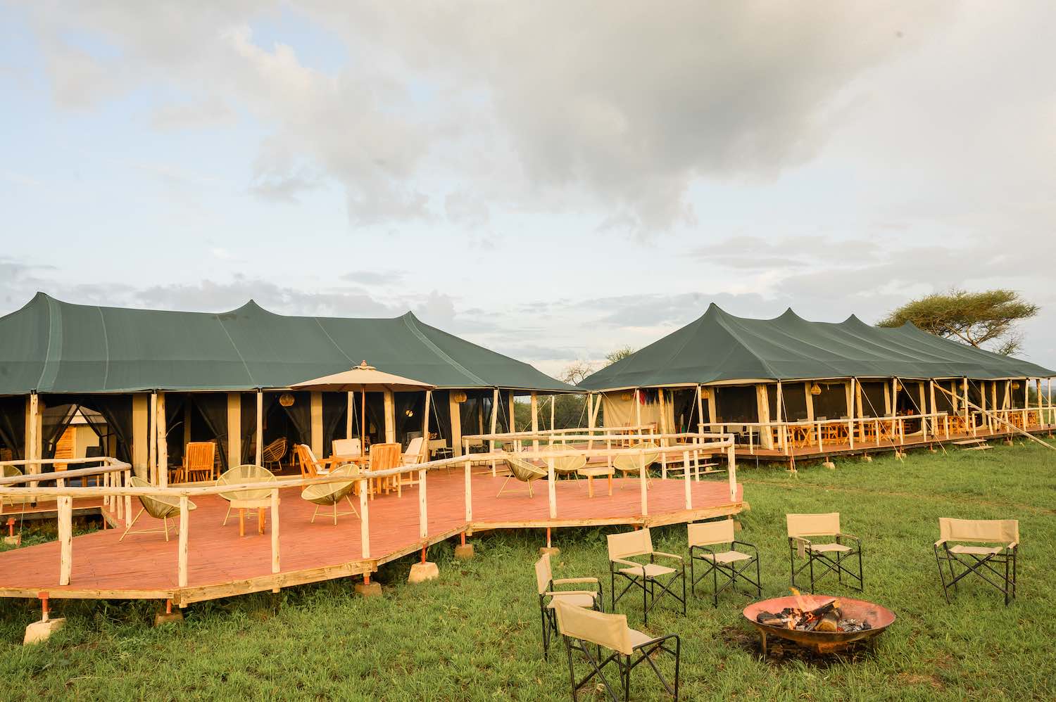 Safari camp with campfire area and outdoor dining setup at golden hour